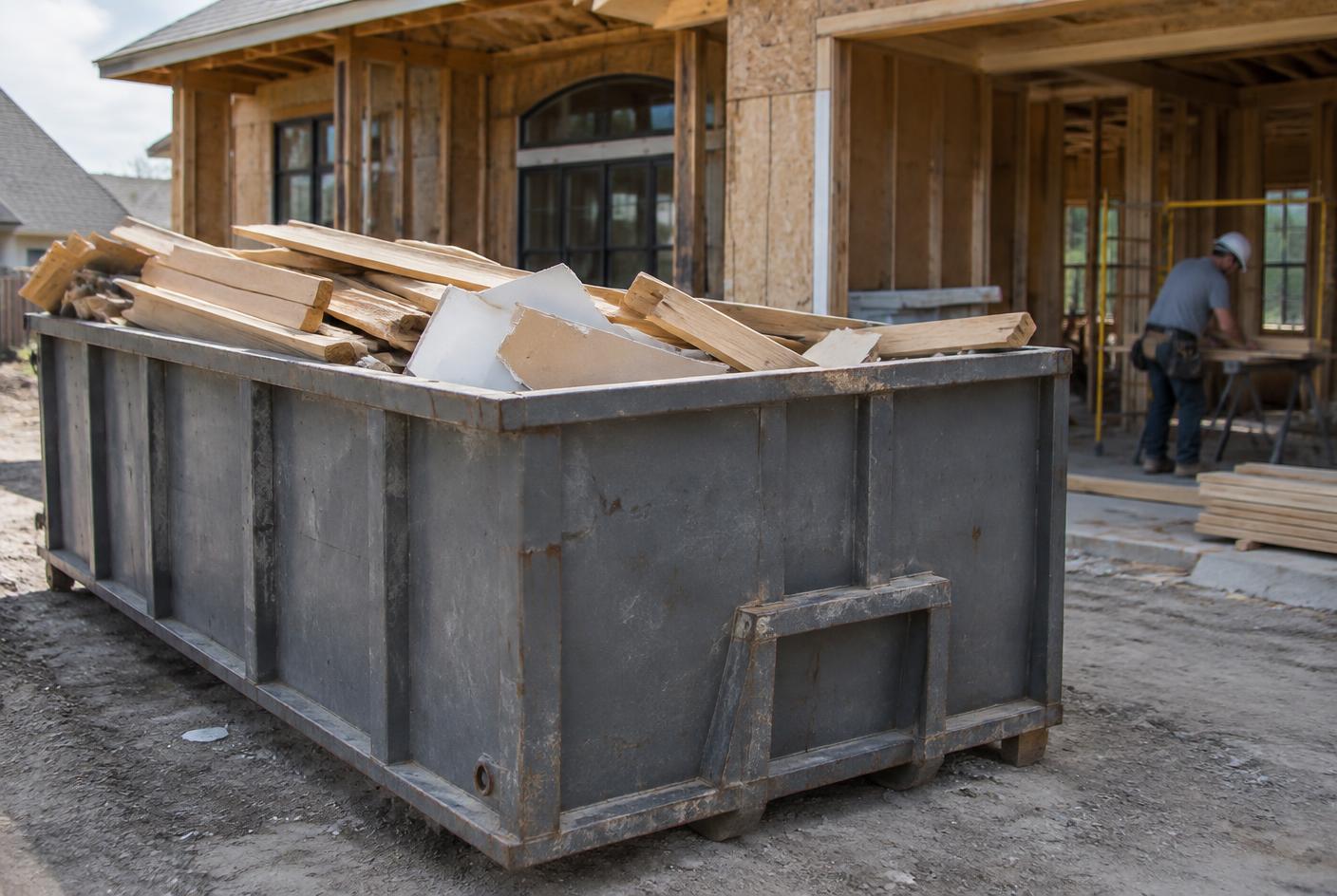Roll-off dumpster holding framing lumber and drywall at an orderly residential construction site