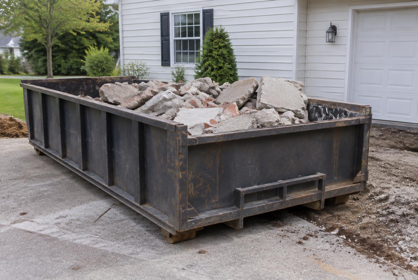 Roll-off dumpster loaded with broken concrete slabs and bricks at a residential driveway project